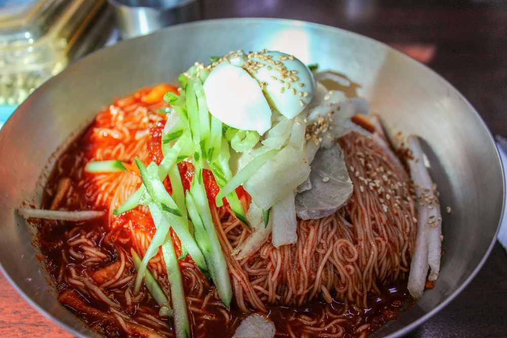 韓国冷麺のビビンネンミョン。コチュジャンベースの甘辛いタレで和えた冷麺がスチールボウルに盛られている。