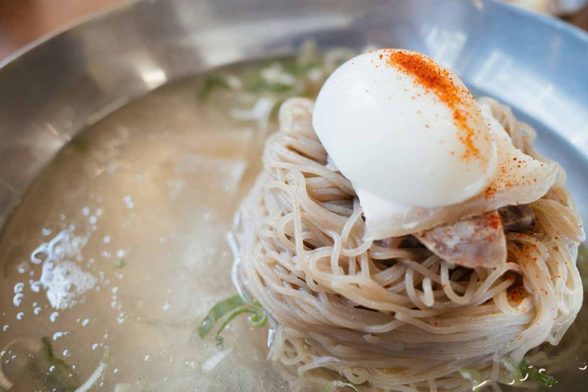 韓国冷麺(ムルネンミョン)。透き通った冷たいスープにそば粉の麺が入り、ゆで卵やキュウリがトッピングされた夏の定番。